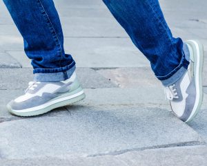 close-up of a woman's feet in jeans and sneakers tripping over unevenly laid paving slabs. Accident, injury on a walk due to poor road surface.